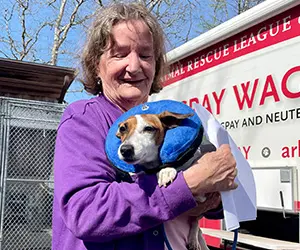 A person holding a small dog in front of the ARL's Spay Waggin