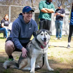 A person kneeling next to a large dog, smiling