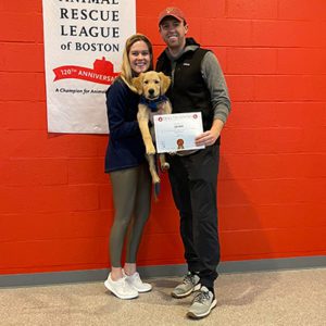 Two people holding a golden retriever with dog training certificate 