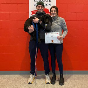 Two people holding a black lab puppy with dog training certificate 