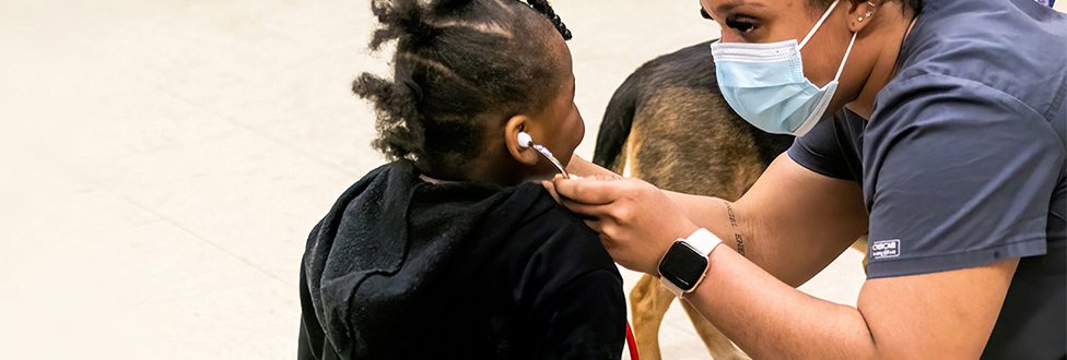 Vet tech with small child, helping with stethoscope