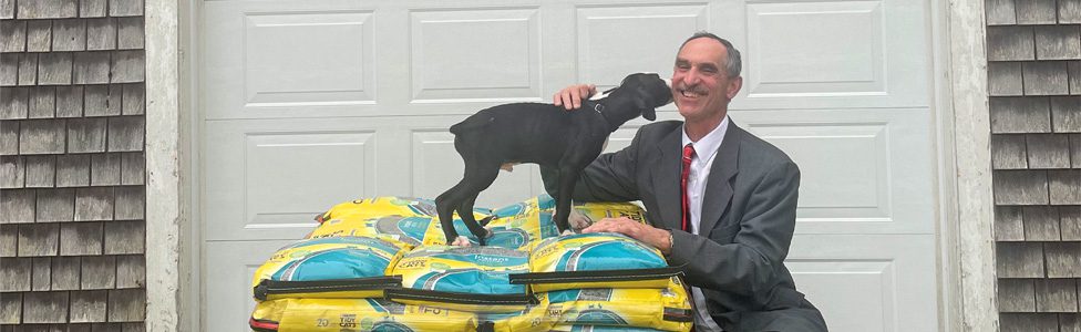 Supporter Spotlight Steve Chapman kneeling down next to a small black puppy on a pile of dog food.