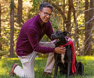A person kneeling down next to a large dog outside, smiling