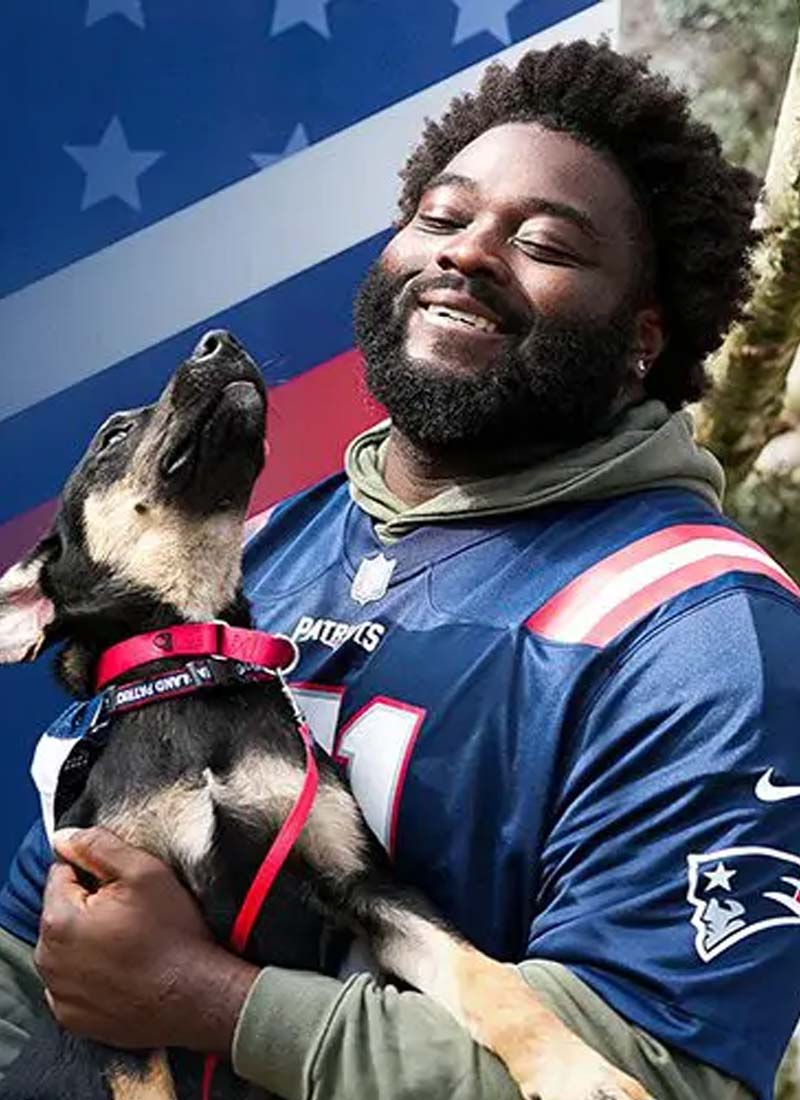 A happy person in a Patriots jersey holds a German Shepherd mix puppy.