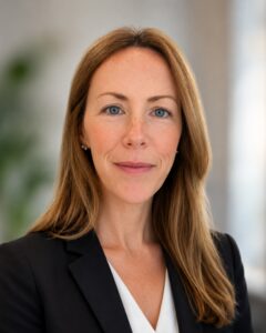 Professional headshot of a smiling woman with long brown hair in a black blazer and white blouse.